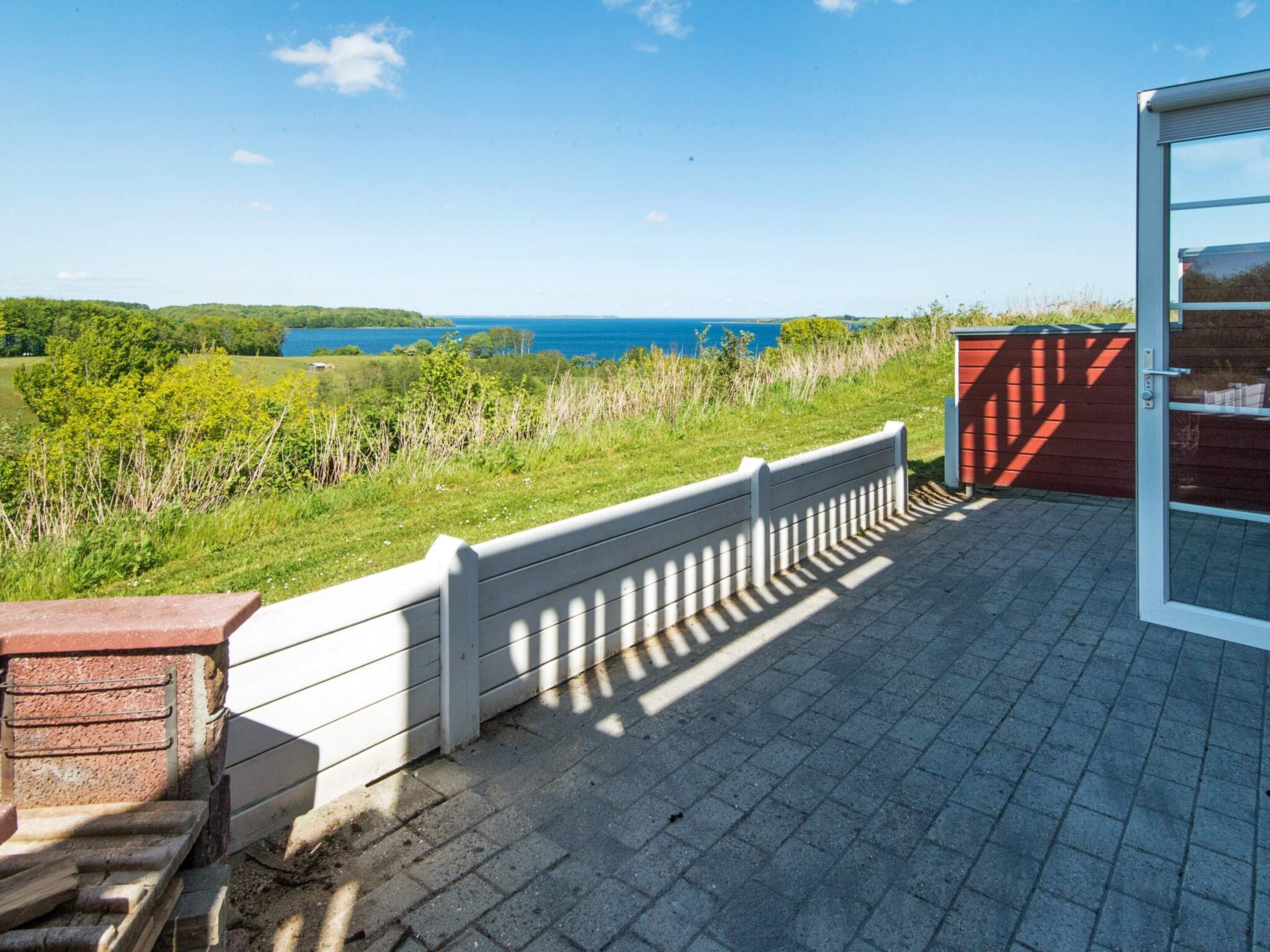 A patio with a view of the sea, a wooden fence, and a red door.