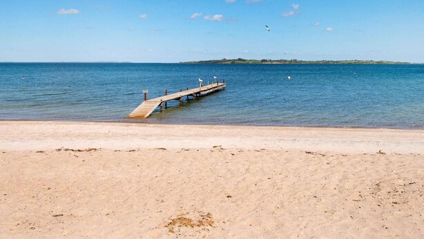 A beach with a wooden pier extending into calm waters, a clear sky, and a distant landmass. - 6 Person Holiday Home in Aabenraa (Aabenraa)