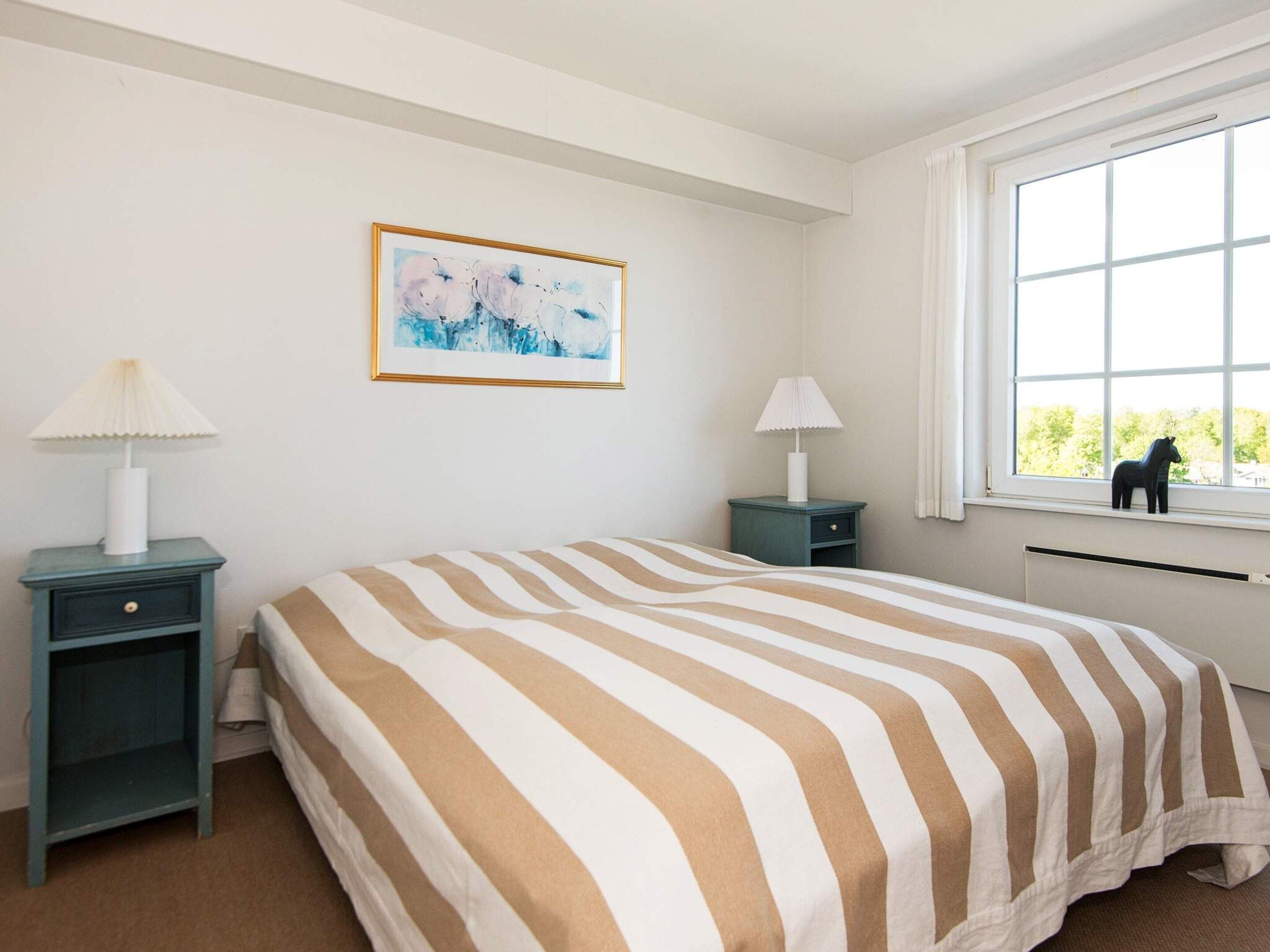 A bedroom with a bed, two bedside tables, a window with a view, and a framed picture on the wall.