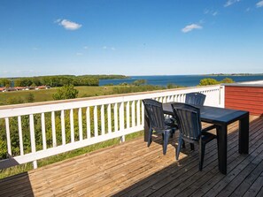 A wooden deck with a white railing, two chairs, and a table overlooking a body of water and distant landscape. - 6 Person Holiday Home in Aabenraa (Aabenraa)