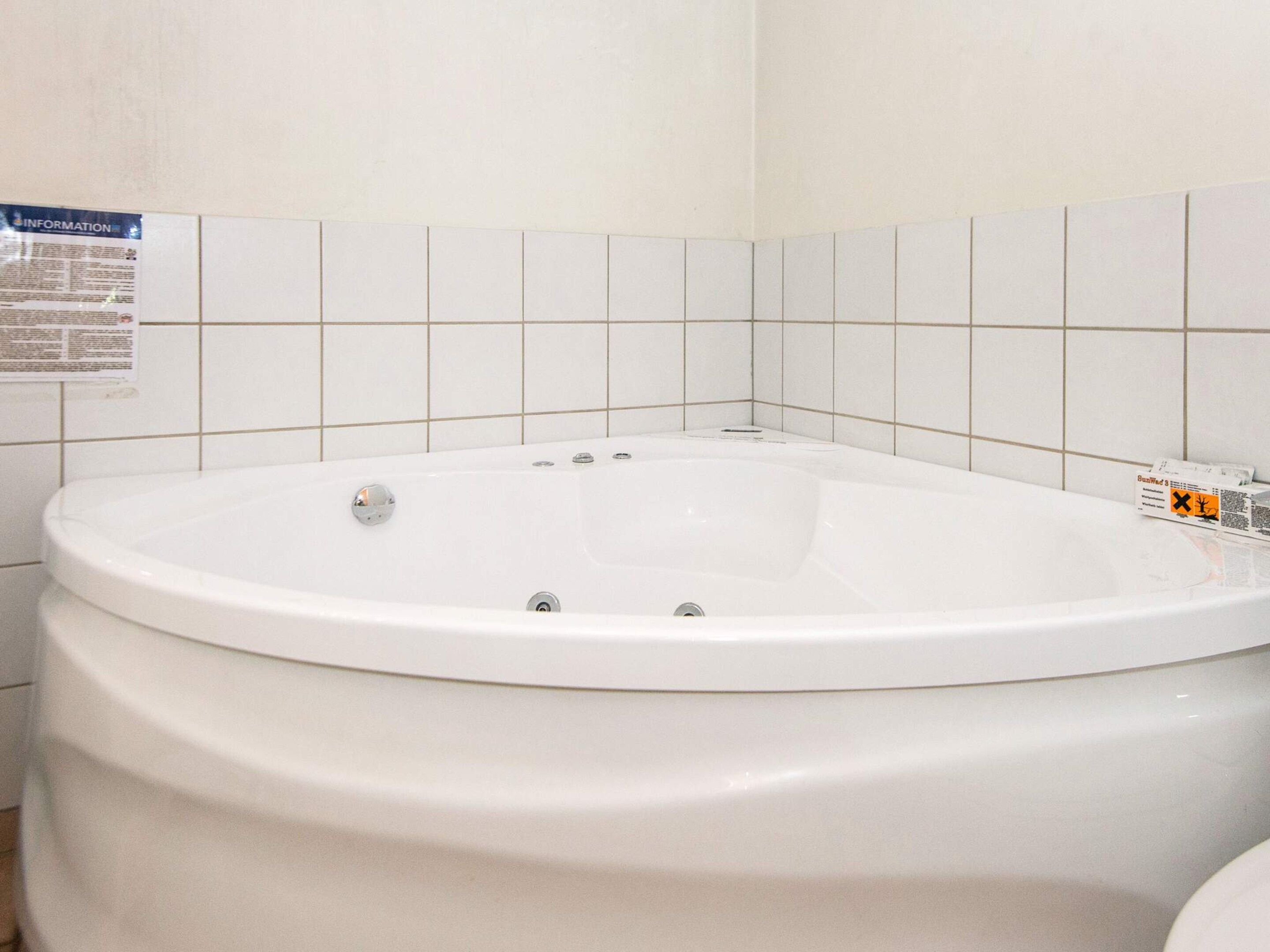 A white bathtub with a control panel, set against a tiled wall with a poster.