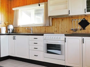 A kitchen with white cabinets, a stove, and a window with curtains.