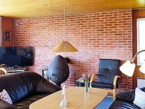 A room with a brick wall, a flat-screen TV, a wooden ceiling, a black leather sofa, a wooden coffee table, and a black chair.