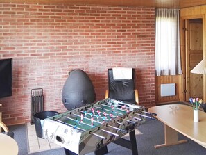 A room with a foosball table, a brick wall, a television, and a window with curtains.