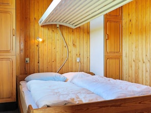 Een kamer met houten lambrisering, een bed, een plafondlamp en een stopcontact.
