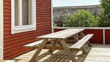 A wooden deck with a picnic table and benches, a window, and a view of a fence and greenery.