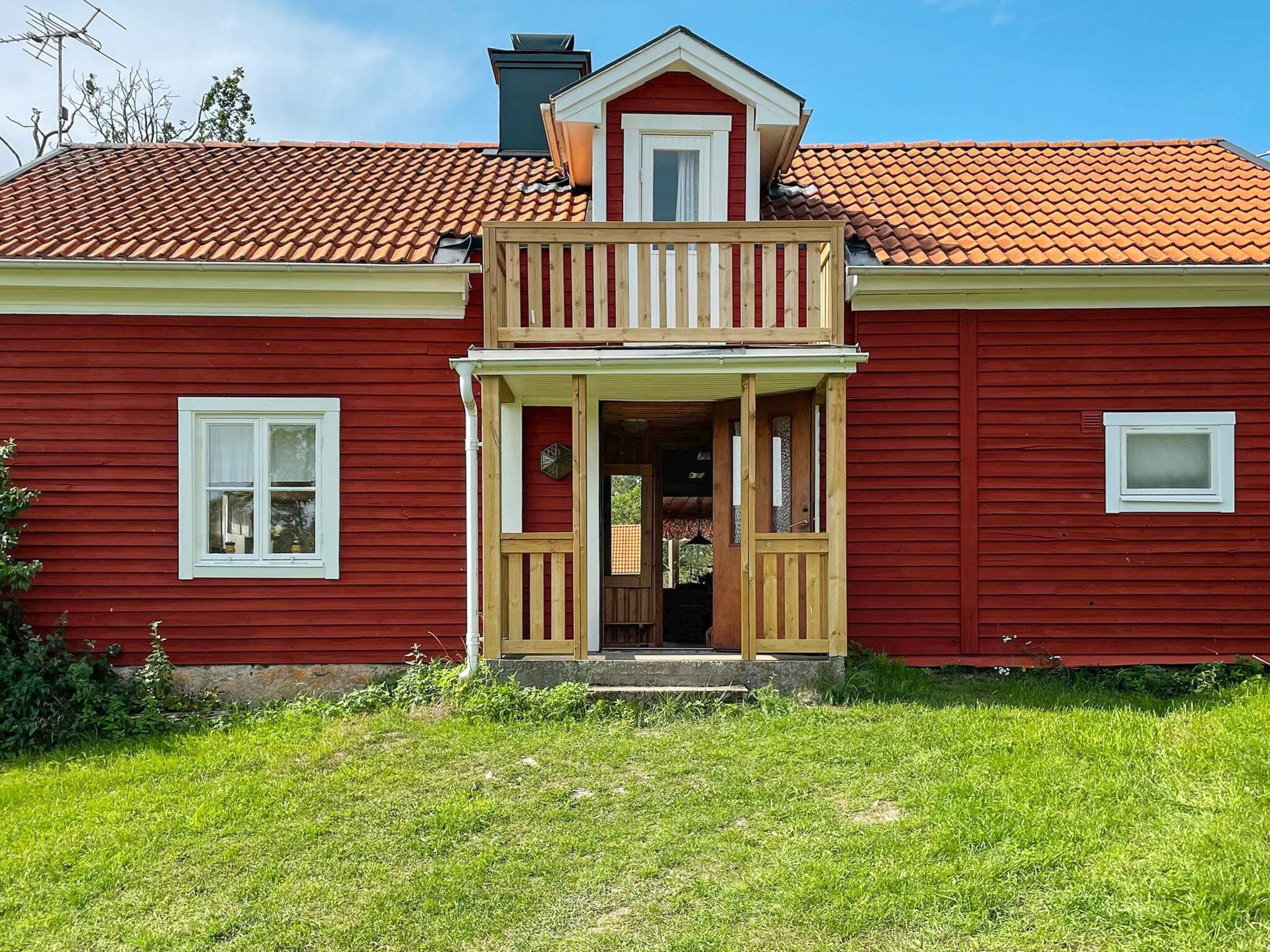 Une maison rouge à deux étages, dotée d’un balcon, d’une cheminée et d’une petite fenêtre.