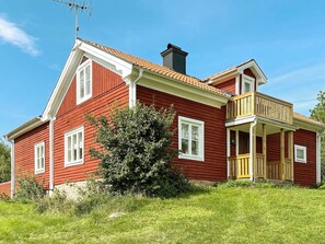 A red wooden house with a balcony, a chimney, and a small tree in front. - 8 Person Holiday Home in Valdemarsvik (Valdemarsvik)