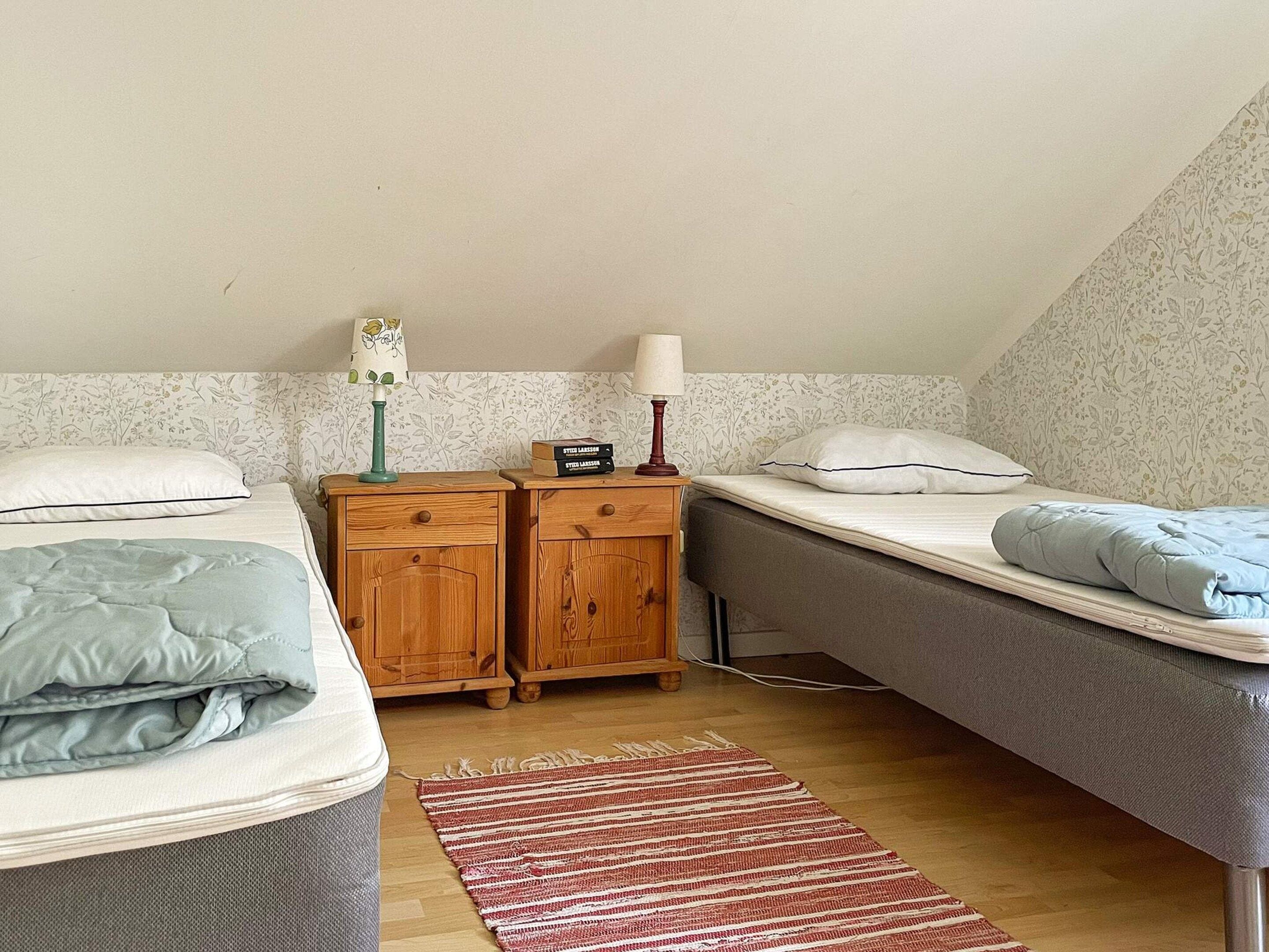Une chambre avec deux lits, une table de chevet en bois, une lampe et un mur décoré d’un motif.