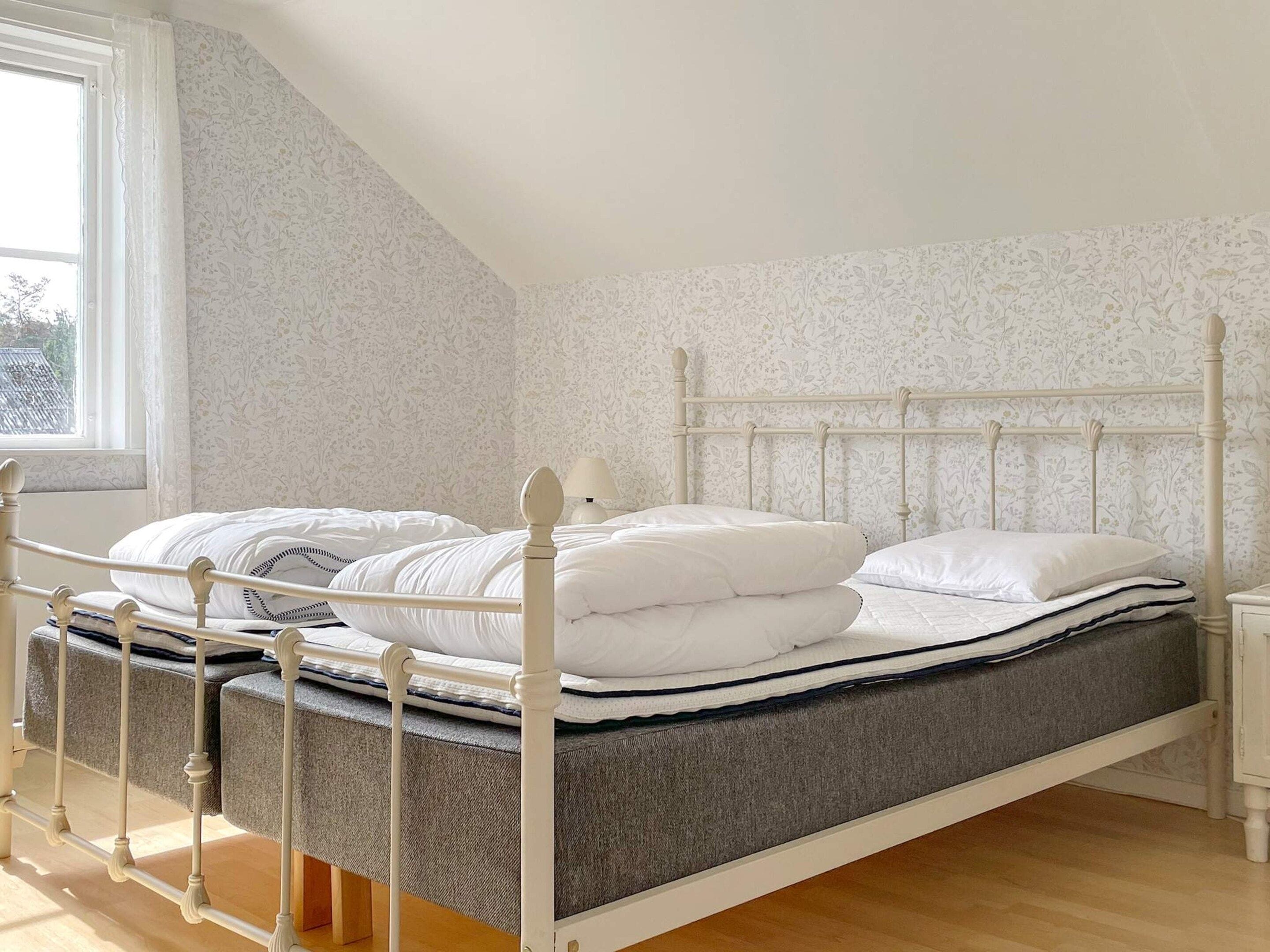 A bedroom with a bed, a nightstand, a window, and a patterned wall.