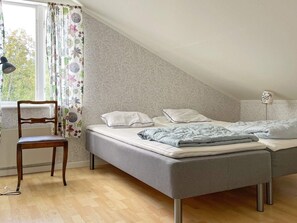 A bedroom with a bed, a chair, a window with curtains, and a lamp. - 8 Person Holiday Home in Valdemarsvik (Valdemarsvik)