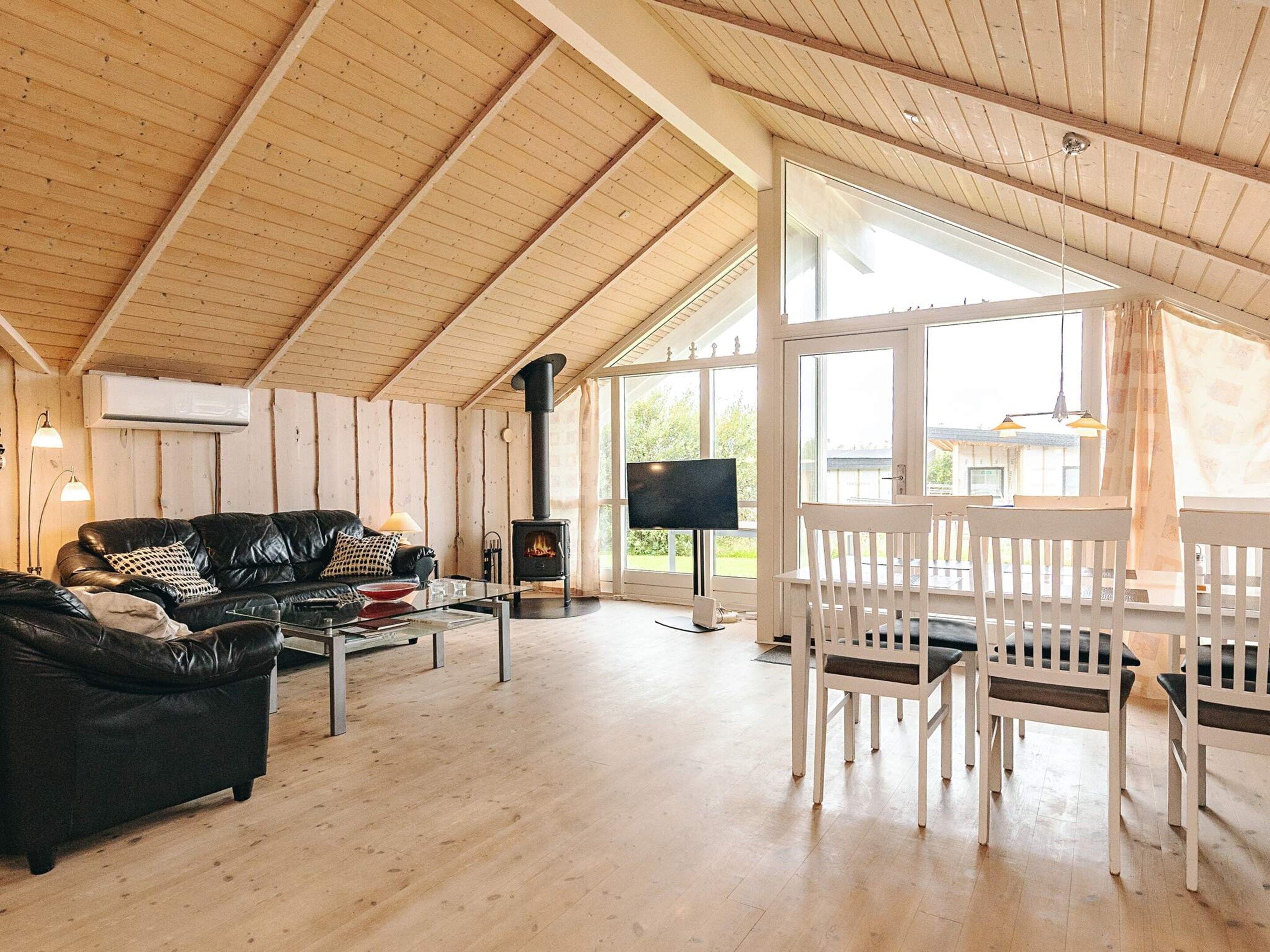 A spacious living area with a wooden ceiling, a black leather sofa, a white dining set, and a fireplace.