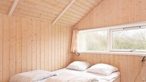 Una cama individual con un edredón y almohadas, una ventana con vistas a árboles y paredes de madera.
