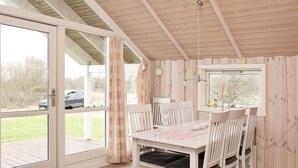 Interior de madera con una mesa y sillas para comer, una ventana con cortinas y una puerta que da al exterior.
