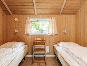 Une chambre avec deux lits, une échelle en bois, une fenêtre avec des rideaux et un radiateur fixé au mur.