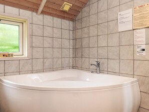 A bathroom with a large bathtub, tiled walls, a window, and informational posters.