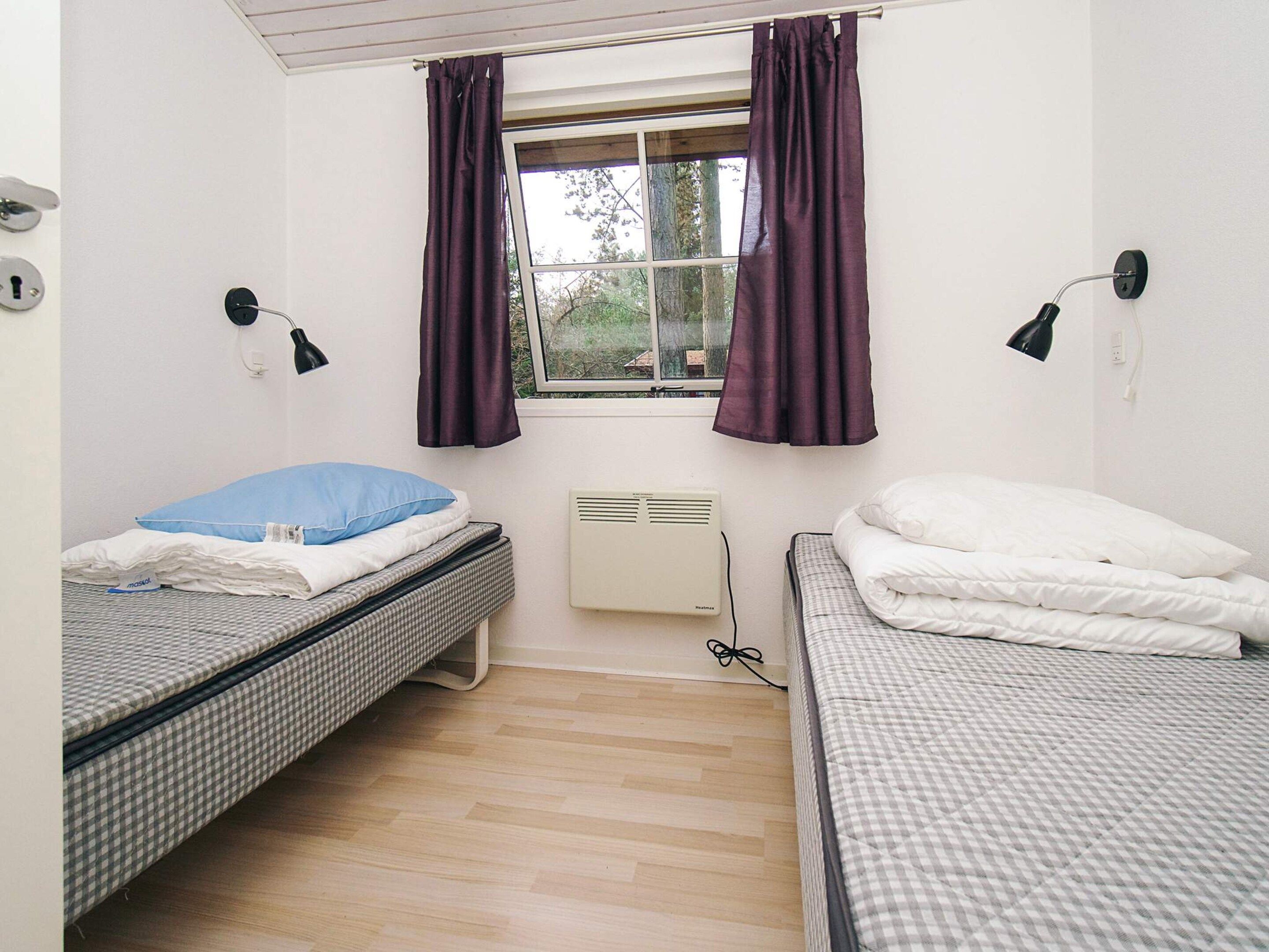 A room with two beds, a window with curtains, a wall-mounted lamp, and a radiator.