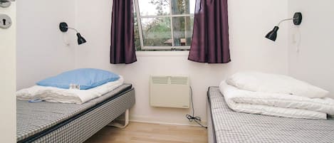 A room with two beds, a window with curtains, a wall-mounted lamp, and a radiator.