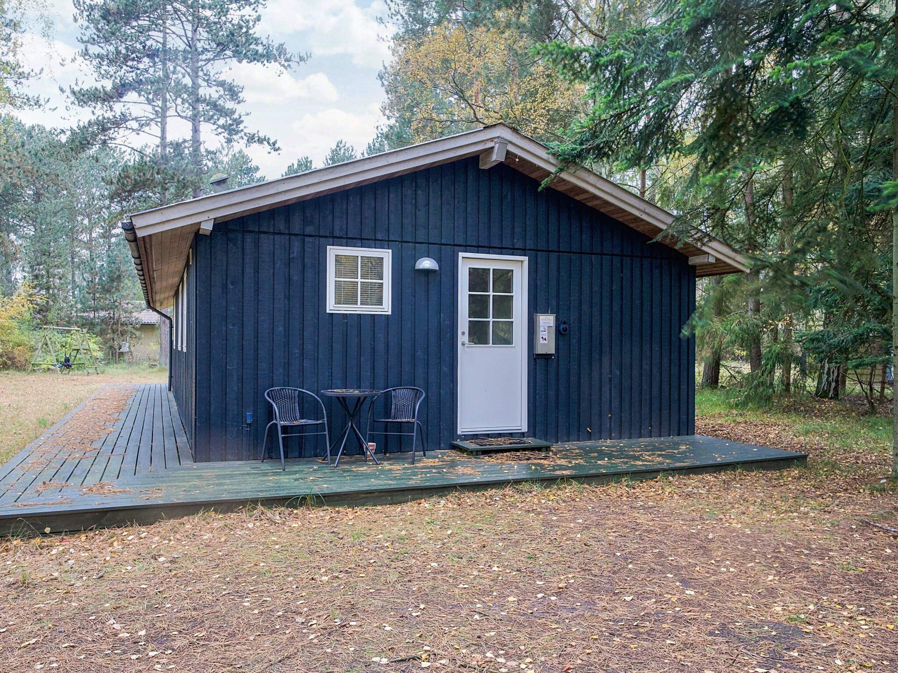 Una piccola baita di legno scuro con un portico, due sedie e una porta.