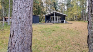 Eine Hütte mit großem Fenster, einer Terrasse und einem kleinen Schuppen in einem Wald.