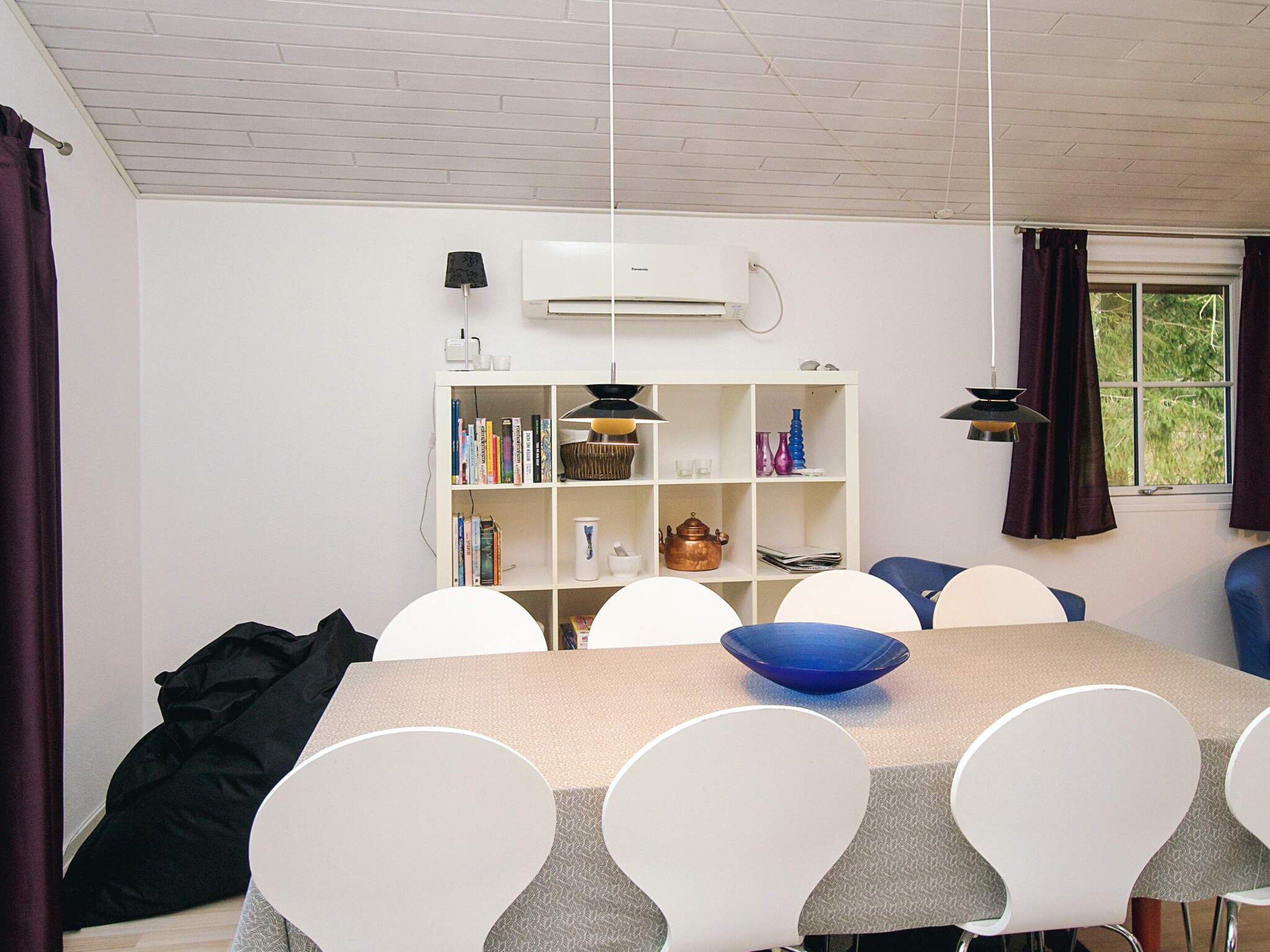 A dining area with a table, chairs, a bookshelf, and a window with curtains.