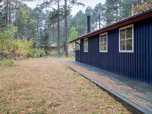 A cabin with a wooden deck and a chimney, surrounded by a forest. - Idyllic Holiday Home in Store Fuglede near Forest (Store Fuglede)