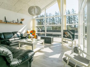 A modern living room with a leather sofa, a glass coffee table, and a television on a stand. - 5 Star Holiday Home in Lokken (Lokken)