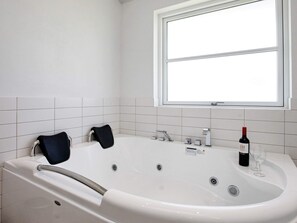 A bathroom with a bathtub, a window, and a bottle of wine on the sink. - 5 Star Holiday Home in Lokken (Lokken)