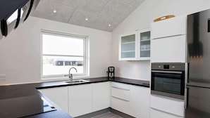A modern kitchen with white cabinets, a black countertop, a built-in oven, and a stainless steel refrigerator.