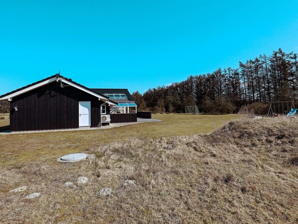 A black building with a white door, a small attached structure, and a grassy field with trees in the background.