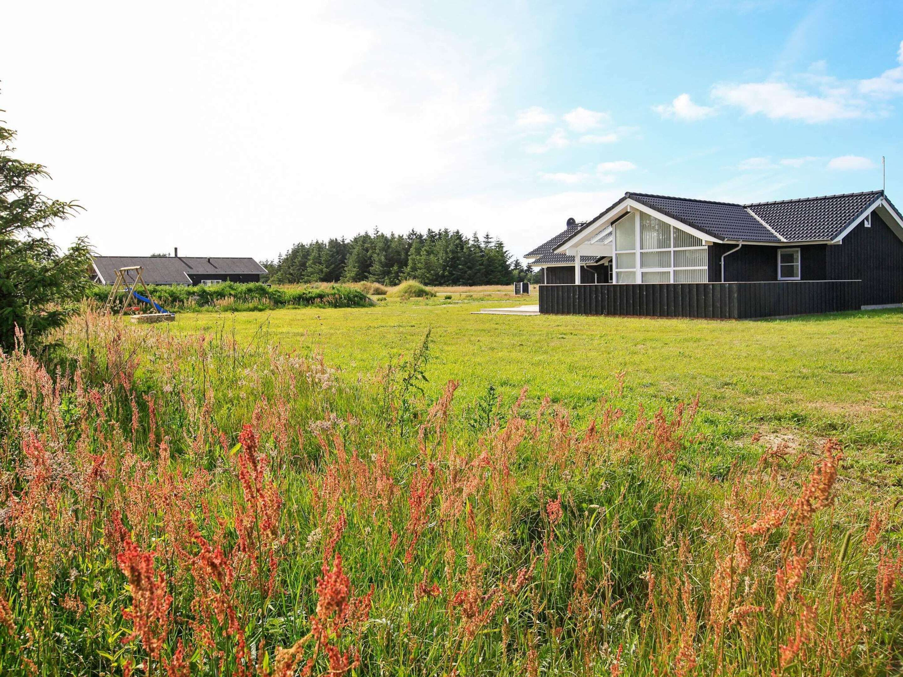 A modern house with a large front yard and a wooden fence.