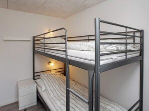 A bunk bed with two levels, a bedside table, and a wall-mounted light.