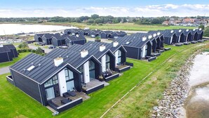 A row of modern, dark-colored cabins with flat roofs, arranged along a grassy area beside a body of water. - 8 Person Holiday Home in Hadsund-by Traum (Hadsund)