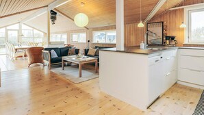 En rummelig opholdsstue med trælofter, et spisebord, sofaer og en køkkenø.