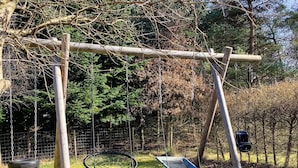 A wooden swing set with two swings and a tire swing in a grassy area with trees in the background. - 5 Star Holiday Home in Skals (Skals)