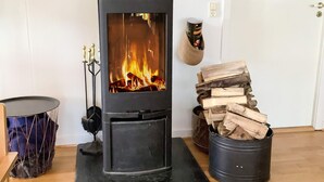 A wood-burning stove with a glass door, a pile of firewood, and a trash bin. - 5 Star Holiday Home in Skals (Skals)