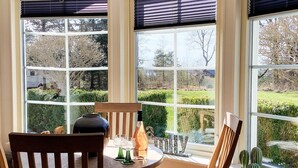 A dining area with a round table, two wooden chairs, and a view of a garden through large windows. - 5 Star Holiday Home in Skals (Skals)