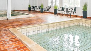 An indoor swimming pool with tiled walls and a brick floor, surrounded by black chairs and potted plants. - 4 Person Holiday Home in Hojer-by Traum (Højer)