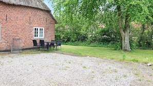 A brick building with a thatched roof, a gravel area, and a table with chairs. - 4 Person Holiday Home in Hojer-by Traum (Højer)