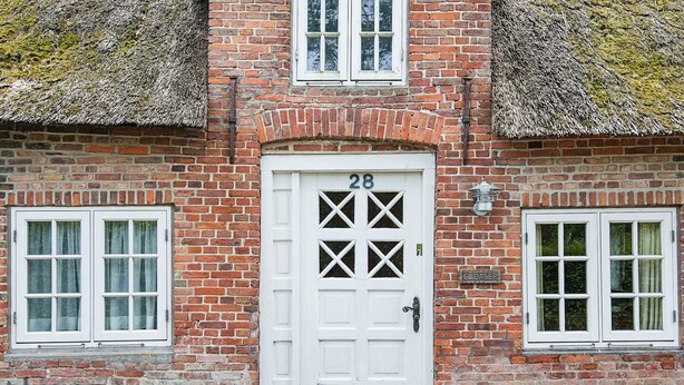 A traditional brick house with a white door marked with the number 28, two windows with white frames, and a small potted plant beside the door. - 4 Person Holiday Home in Hojer-by Traum (Højer)