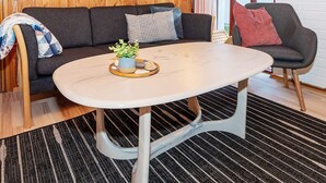 Une pièce chaleureuse avec un mur en bois, un canapé gris foncé, une table ronde blanche et une petite plante en pot.
