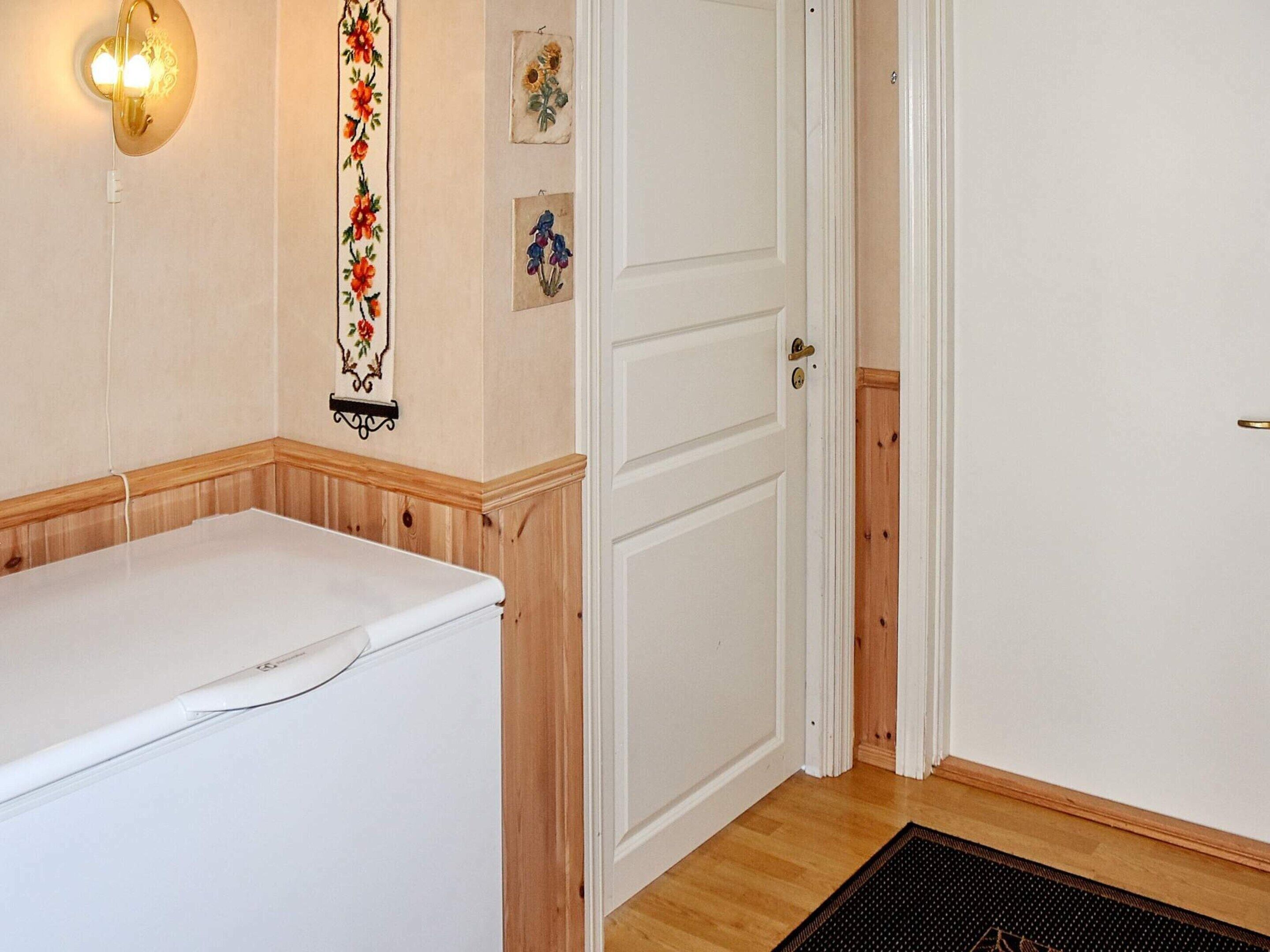 A room with a white wall, a wooden bench, a white door, and a wall-mounted light fixture.