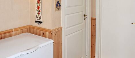 A room with a white wall, a wooden bench, a white door, and a wall-mounted light fixture.