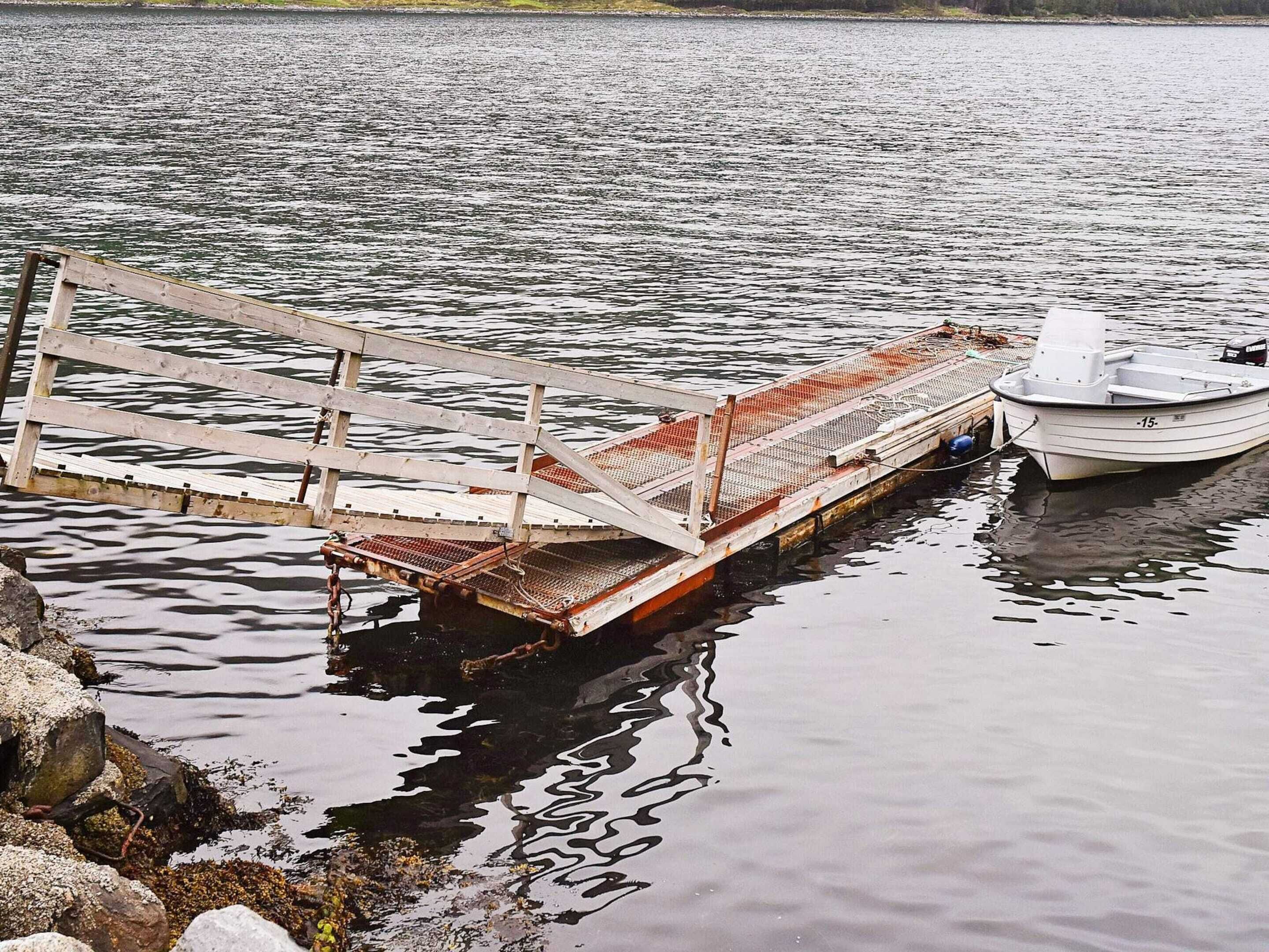 A dock with a boat moored beside it, a wooden pier extending into the water, and a rocky shoreline.