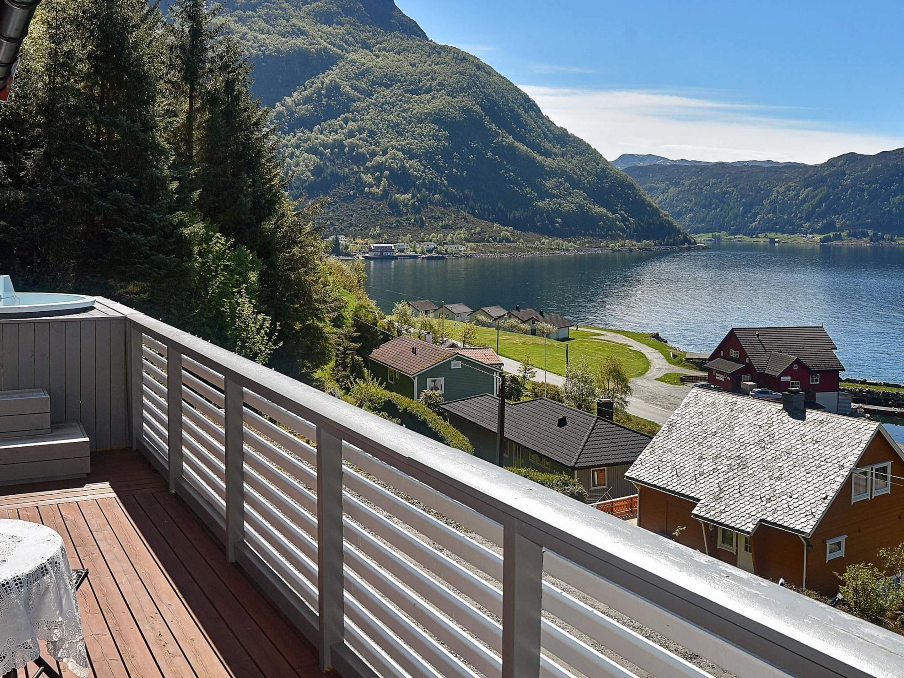 A wooden deck with a table, overlooking a lake with houses and mountains in the background.