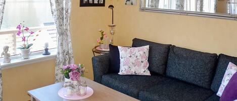 A cozy living room with a sofa, a coffee table, a chandelier, and a large window with curtains.