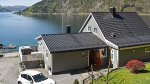 Een huis aan een meer met een steiger, een auto en een berg op de achtergrond.