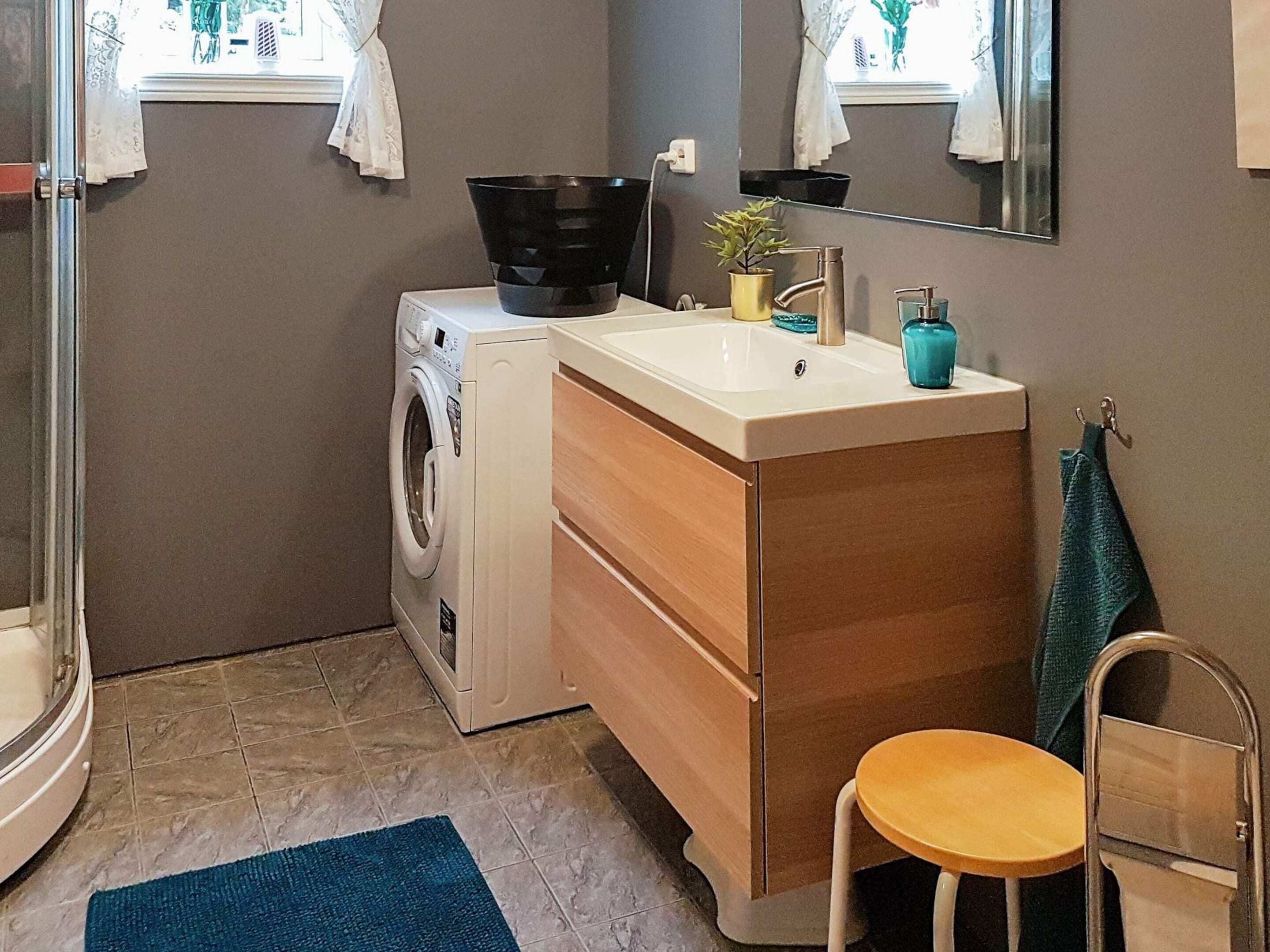 Ein kleines Badezimmer mit Waschmaschine, Waschbecken, Spiegel und einer kleinen Hocker.