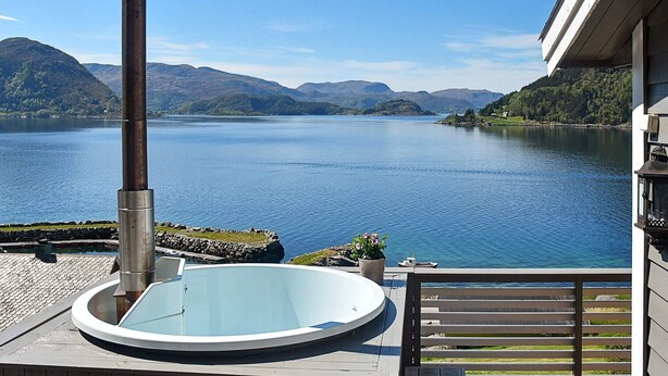 Een hottub op een terras met uitzicht op een meer, met bergen op de achtergrond.