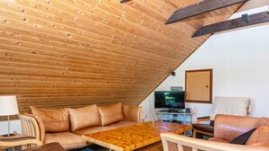 A cozy, sloped-roof room with a wooden ceiling, a sofa, a small table, and a television.
